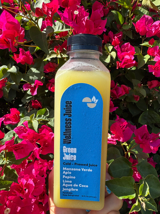 Bottle of wellness juice with a blue label held in front of pink flowers
